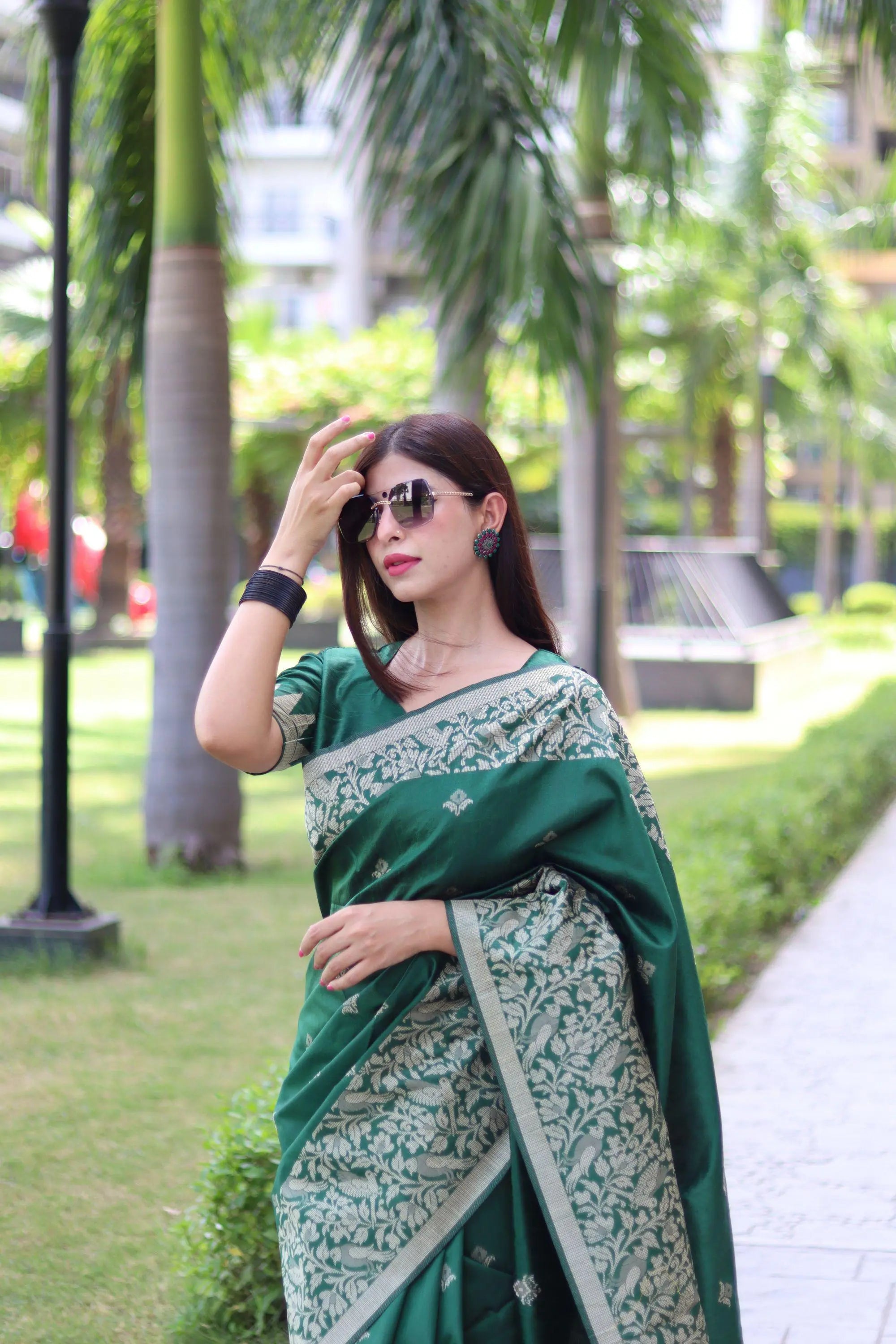 Woman in deep green traditional weaving saree standing elegantly in a garden with palm trees